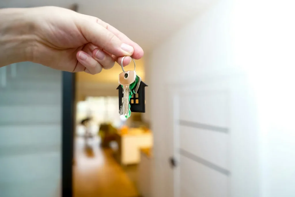 Hand holding house keys at an open front door